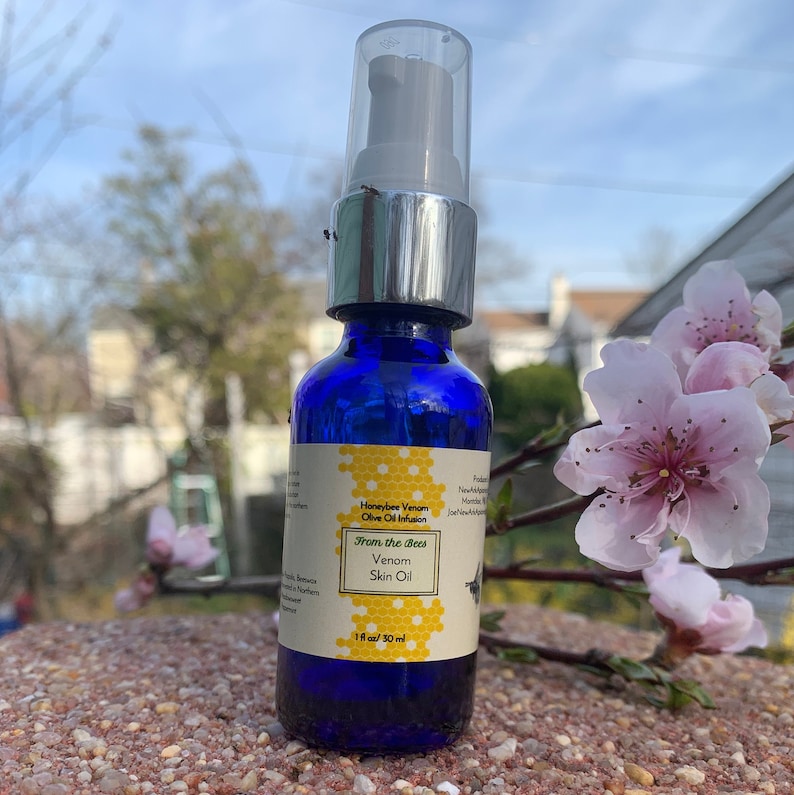 May include: A blue glass bottle with a silver pump top and a white label. The label says "Honeybee Venom Olive Oil Infusion From the Bees Venom Skin Oil 1 fl oz / 30 ml".