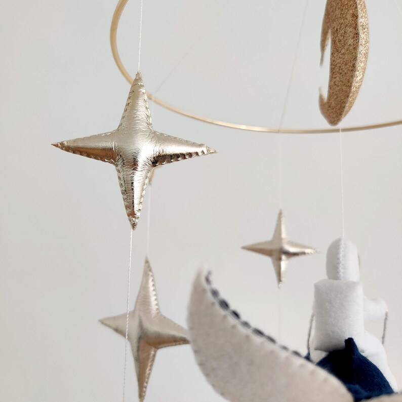 May include: A gold and white mobile with a crescent moon, stars, and a cloud. The mobile is hanging from a gold hoop.