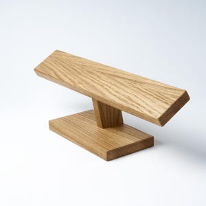 May include: A wooden stand for displaying bracelets. The stand is made of light brown wood and has a simple, modern design.