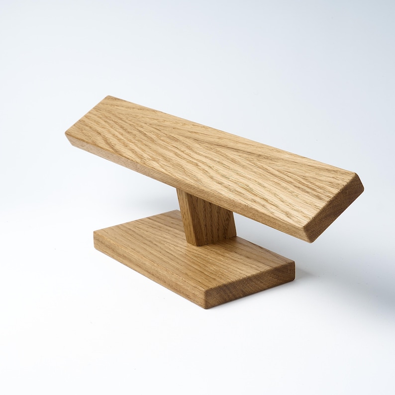 May include: A wooden stand for displaying bracelets. The stand is made of light brown wood and has a simple, modern design.