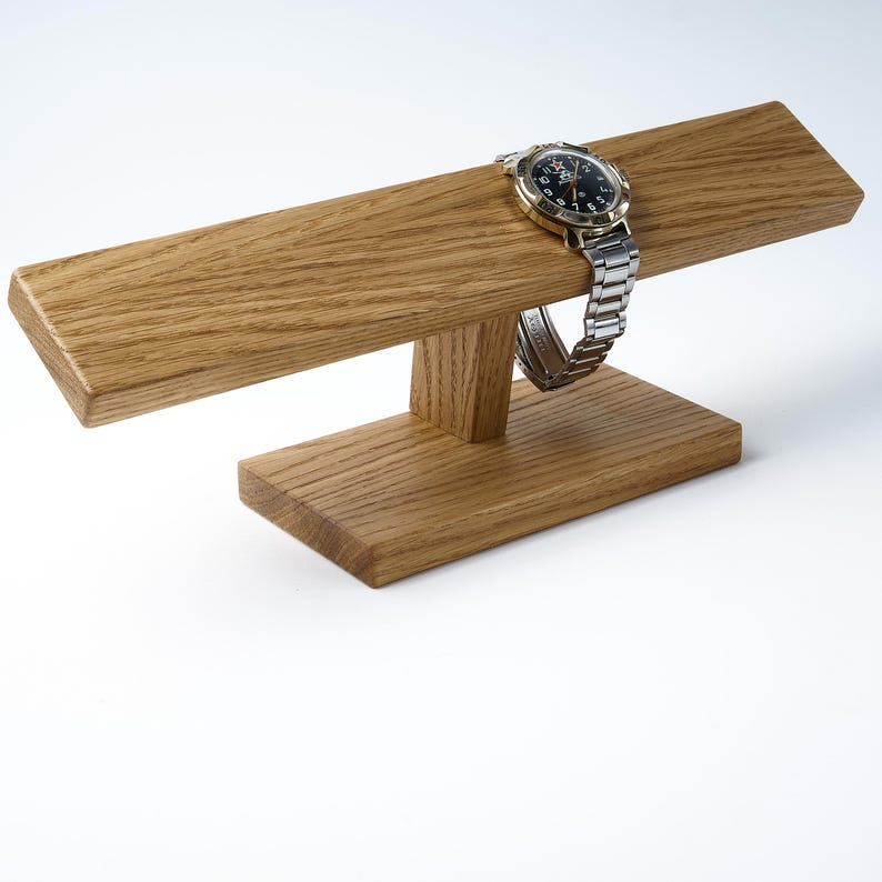 May include: A wooden watch stand with a watch on it. The stand is made of light brown wood and has a simple design. The watch is silver with a black face.