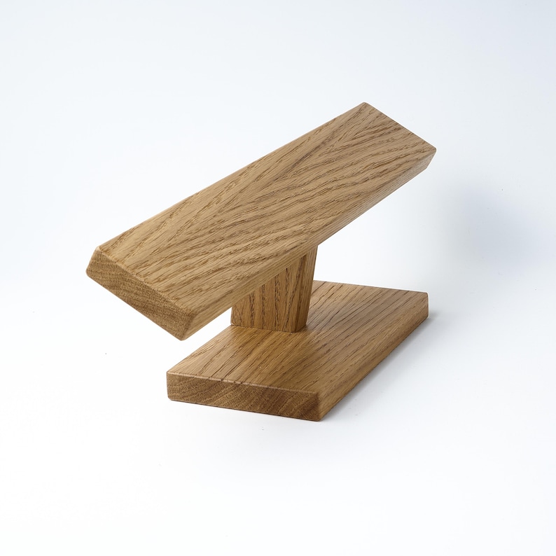 May include: A wooden stand for displaying bracelets or watches. The stand is made of light brown wood and has a simple, modern design.