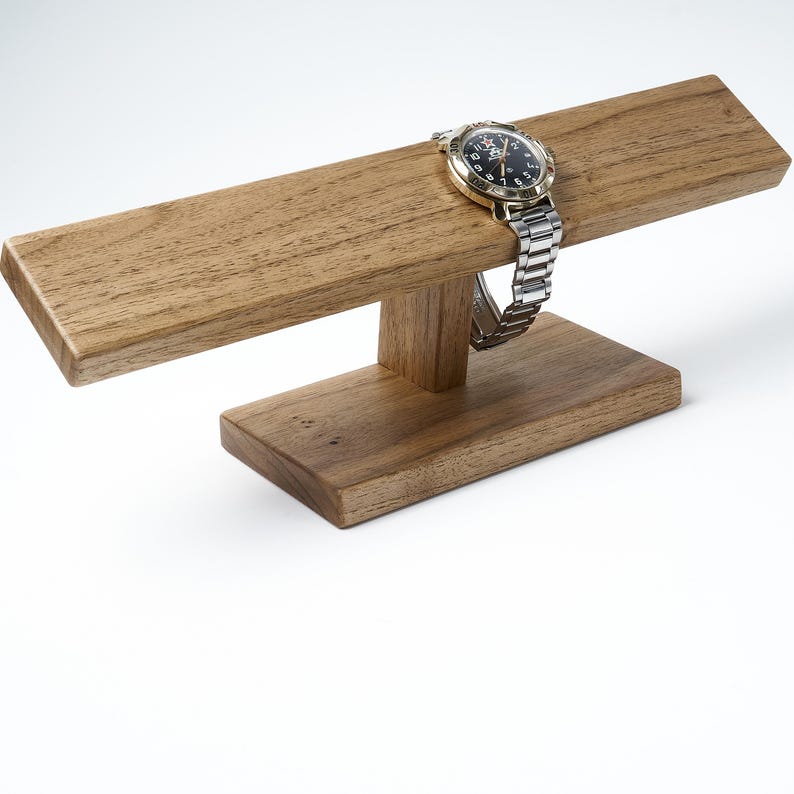 May include: A wooden watch stand with a watch on it. The stand is made of light brown wood and has a rectangular base and a curved top.