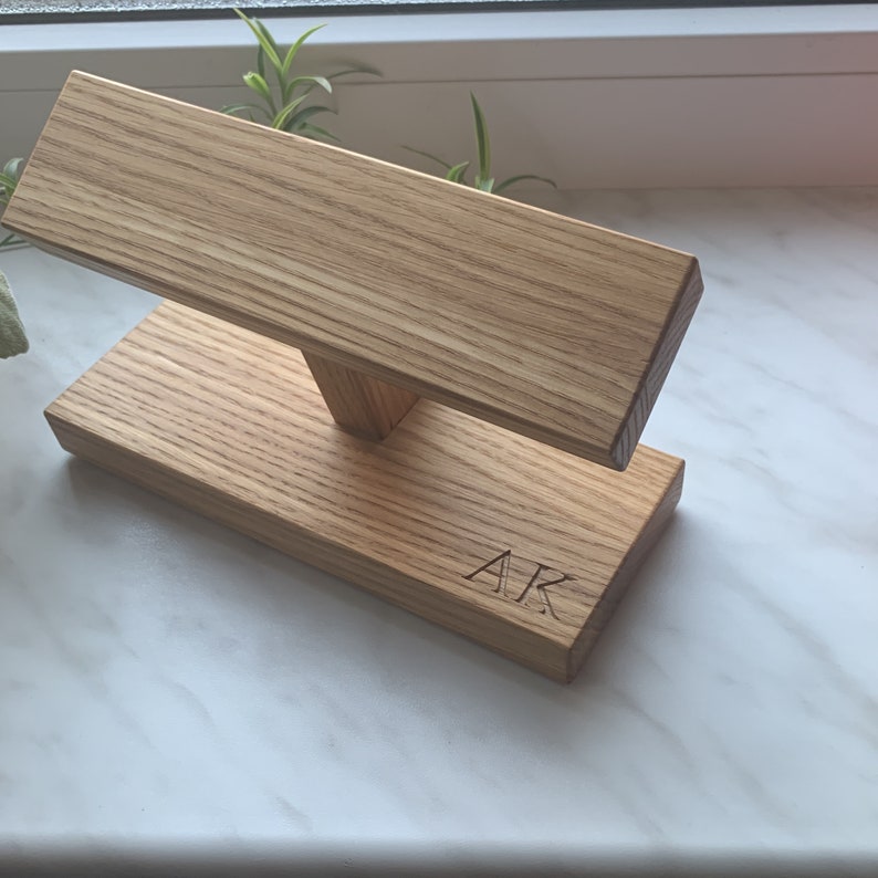 May include: A wooden stand for displaying bracelets or watches. The stand is made of light brown wood and has a simple design. The stand is engraved with the initials "AR".