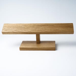 May include: A wooden stand with a rectangular top and a T-shaped base. The stand is made of light brown wood with a natural grain.