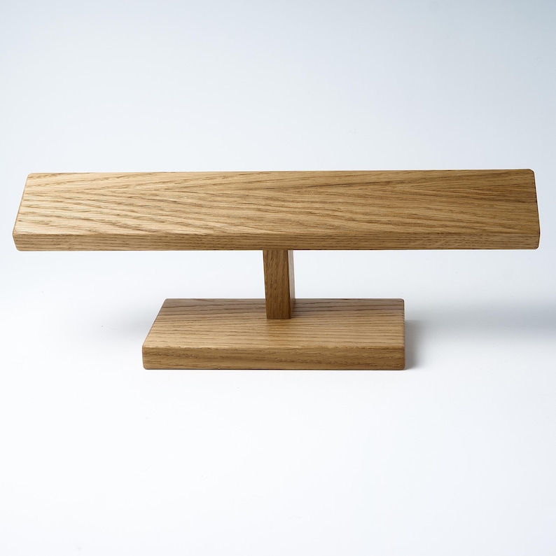 May include: A wooden stand with a rectangular top and a T-shaped base. The stand is made of light brown wood with a natural grain.