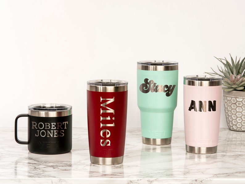May include: Four personalized insulated tumblers and a mug with names engraved. The tumblers are in black, red, mint green, and pink. The mug is black. The names are "Robert Jones", "Miles", "Stacy", and "Ann".
