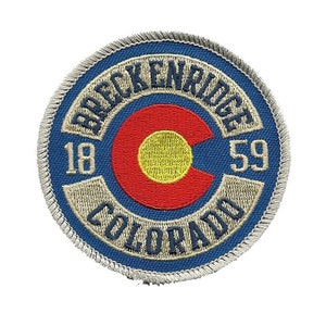 May include: A blue and white embroidered patch with the text "Breckenridge Colorado 18 59" and a red, yellow, and white Colorado state flag in the center.