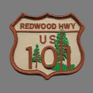 May include: A brown and white embroidered patch with the text "Redwood Hwy US 101". The patch features two green trees and a brown outline.