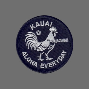May include: A navy blue circular patch with white embroidered text and a rooster illustration. The text reads "KAUAI", "HAWAII", and "ALOHA EVERYDAY". The rooster is depicted in a detailed, stylized manner.