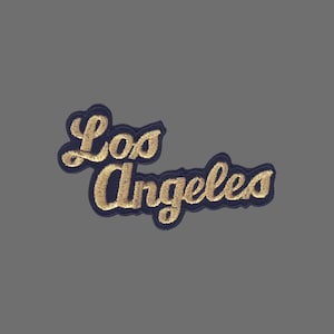 May include: Embroidered patch featuring the text "Los Angeles" in a cursive script. The lettering is gold, with a navy blue border and backing. The patch is designed for application on clothing or accessories.