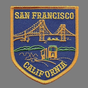 May include: A blue and gold embroidered patch with the text "SAN FRANCISCO CALIFORNIA" and an image of the Golden Gate Bridge and a cable car.