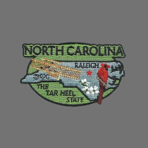May include: Embroidered patch featuring a green outline of North Carolina with a red cardinal bird, the text "North Carolina", "The Tar Heel State", and "Raleigh" inside the outline.
