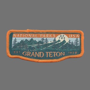 May include: Orange and green embroidered patch with the text "National Parks of the USA" and "Grand Teton" with the dates "Est. 1929".