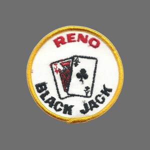May include: Embroidered patch with a white background and a gold border. The patch features the word "RENO" in red, and the words "BLACK JACK" in black. Two playing cards are in the center.