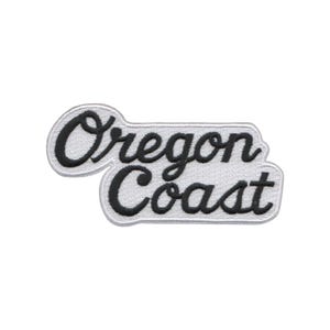 May include: Embroidered patch with the words "Oregon Coast" in a cursive font. The text is black with a white border, set against a light gray background. The patch has a rectangular shape with rounded corners.