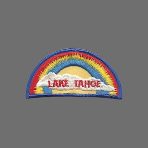 May include: Embroidered patch featuring a rainbow design with the text "LAKE TAHOE" in red letters. The patch has a blue border and a yellow sun in the center. The rainbow includes red, yellow, and blue colors.
