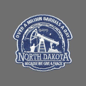 May include: Embroidered patch with a blue and white design. The patch features the text "OVER A MILLION BARRELS A DAY" and "NORTH DAKOTA BECAUSE WE GIVE A FRACK". The image includes an oil pump and a person.