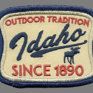 May include: A blue and white embroidered patch with the text "Outdoor Tradition Idaho Since 1890" and a silhouette of a moose.