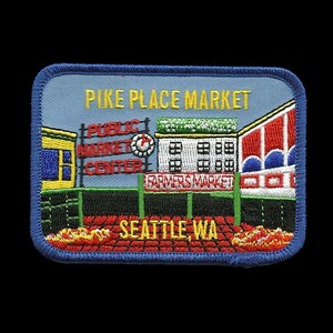 May include: Embroidered patch depicting Pike Place Market in Seattle, Washington. The patch features a blue background with the text "Pike Place Market" in yellow lettering. The patch also includes a depiction of the market's iconic buildings, including the Public Market Center and the Farmers Market.