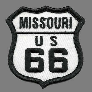 May include: A white and black embroidered patch with the text "Missouri U.S. 66" in a shield shape.