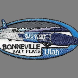 May include: Embroidered patch featuring a blue and white race car design with the text "THE BLUE FLAME" and "BONNEVILLE SALT FLATS Utah" in white lettering. The patch has a blue oval border.