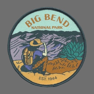 May include: A round, green, embroidered patch with the text "Big Bend National Park" in brown lettering. The patch features a hiker with a backpack looking out at a mountain range. The text "Est. 1944" is at the bottom of the patch.