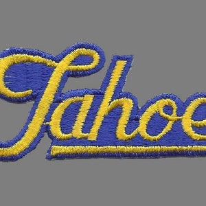 May include: Embroidered patch with the word "Tahoe" in a cursive script. The lettering is yellow, outlined with a blue border. The patch is rectangular and has a gray background.