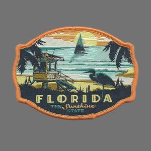May include: An orange, blue, and green embroidered patch with a sunset scene, a beach, a lifeguard stand, a bird, and the text "Florida The Sunshine State".
