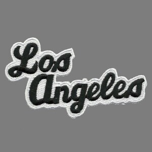 May include: Embroidered patch with the words "Los Angeles" in a cursive script. The black text has a white border, set against a grey backdrop. The patch is designed for application on clothing or accessories.