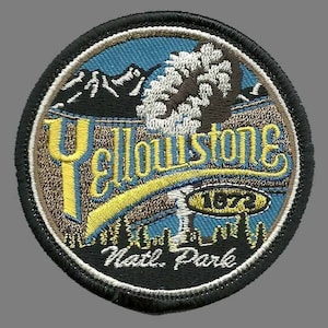 May include: A round, black and white embroidered patch with the words "Yellowstone Natl. Park" and "1872" in yellow. The patch features a blue sky, a mountain range, a tree, and a yellow banner.