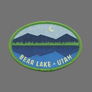 May include: Green oval embroidered patch with a blue and white nighttime scene of mountains, a lake, and a crescent moon. The text "BEAR LAKE * UTAH" is in yellow.