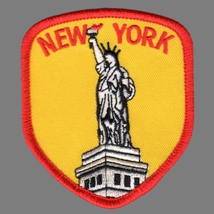 May include: Embroidered patch featuring the Statue of Liberty in white, with a yellow background and red trim. The text "NEW YORK" is arched above the statue in red. The patch is shield-shaped.