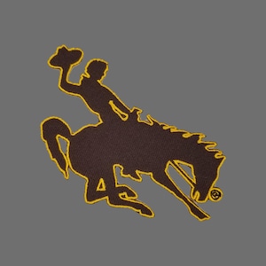 May include: A brown embroidered patch of a cowboy riding a bucking horse. The patch is outlined in yellow thread.