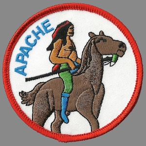 May include: Embroidered patch with a Native American riding a brown horse. The patch is circular with a red border and the word "APACHE" in blue. The Native American figure is wearing a red headband, green pants, and blue boots.