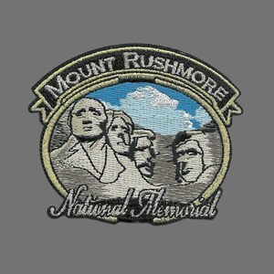 May include: An embroidered patch featuring Mount Rushmore National Memorial. The patch is black with a gold outline and depicts the four presidents carved into the mountain. The text "Mount Rushmore National Memorial" is embroidered in white.