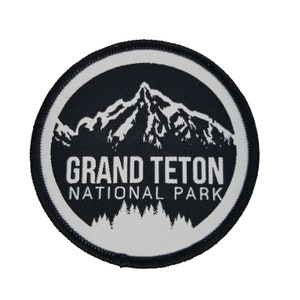 May include: A white and black embroidered patch with a mountain silhouette and the text "Grand Teton National Park".
