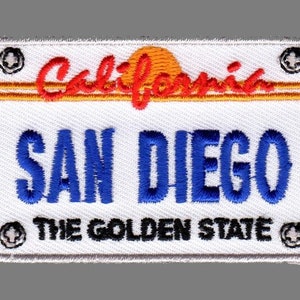 May include: Embroidered patch in the shape of a California license plate. The patch features the word "California" in red script above the blue text "SAN DIEGO". Below, the text "THE GOLDEN STATE" is displayed. The patch has a white background with a gray border.