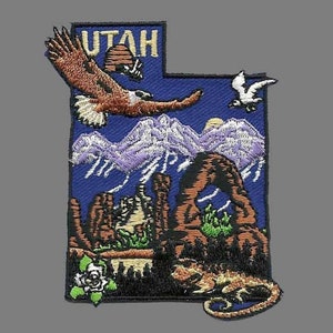 May include: Embroidered patch in the shape of Utah, featuring an eagle, mountains, and desert landscapes. The word "UTAH" is at the top. Includes a desert lizard, a rose, and a flying bird. The patch is on a blue background.