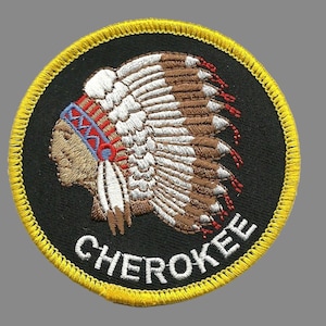 May include: Embroidered patch featuring a Native American chief in profile wearing a headdress. The patch is circular with a black background and a yellow border. The word "CHEROKEE" is embroidered in white.