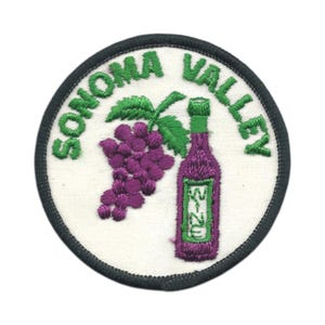 May include: Embroidered patch with the words "SONOMA VALLEY" in green. The patch features a purple grape cluster, a green-topped purple wine bottle, and a green label that says "WINE". The patch has a white background and a dark green border.