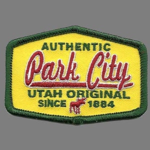 Peut inclure: Un écusson brodé vert et jaune avec le texte "Authentic Park City Utah Original Since 1864" et une illustration stylisée d'une vache rouge.