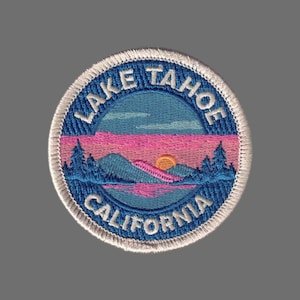 May include: Embroidered patch featuring a scenic Lake Tahoe landscape. The design includes a blue lake, pink and orange sunset, and the text "Lake Tahoe California" in a circular border. The patch has a white border.