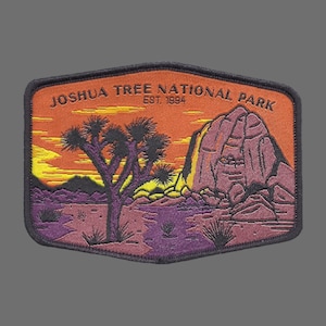 May include: A brown and black embroidered patch with a sunset scene of a Joshua Tree National Park, featuring a Joshua Tree, a rock formation, and the text "Joshua Tree National Park Est. 1994".