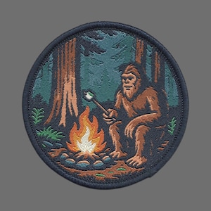 May include: Round patch featuring a brown Bigfoot figure roasting a marshmallow over a campfire in a forest setting. The patch has a dark blue border and includes trees and foliage in shades of green and brown.