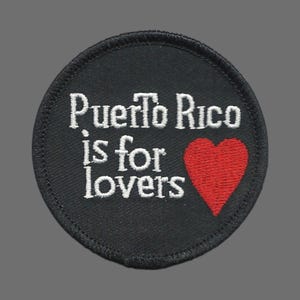 May include: Round black patch with white embroidered text that reads "Puerto Rico is for lovers." A red heart is embroidered to the right of the text. The patch has a black stitched border.