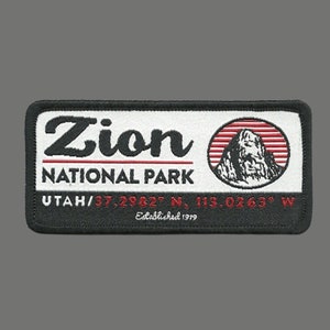 May include: Black and white embroidered patch with red accents. The patch features the text "Zion National Park" and the coordinates "UTAH/ 37.2982° N, 113.0263° W". The text "Established 1919" is also included.
