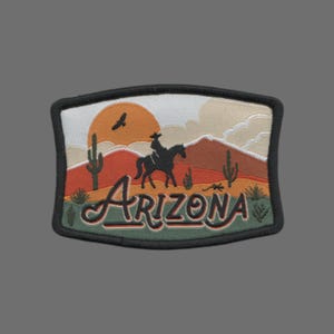 May include: Embroidered patch with a sunset scene, a cowboy riding a horse, and the word "ARIZONA" in a green, cursive font. The patch has a black border and a green background.