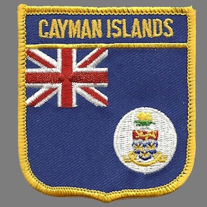 May include: Embroidered patch featuring the words "CAYMAN ISLANDS" in gold lettering above a blue background. The patch includes the Union Jack flag and a circular emblem with a crest, all bordered by gold stitching.