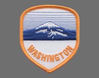 May include: Embroidered patch featuring a mountain landscape with a snow-capped peak and blue mountains. The patch has an orange border and the word "WASHINGTON" in orange lettering.